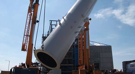 Orange crane lifting a large section of a steel chimney