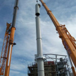 2 cranes installing sections of a steel chimney
