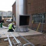 Man inspecting bottom bolts at base of steel chimney