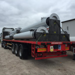 6 sections of a steel chimney getting transported on the back of a flatbed truck