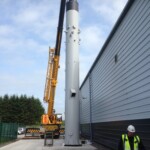 Crane placing a new chimney using heavy chains